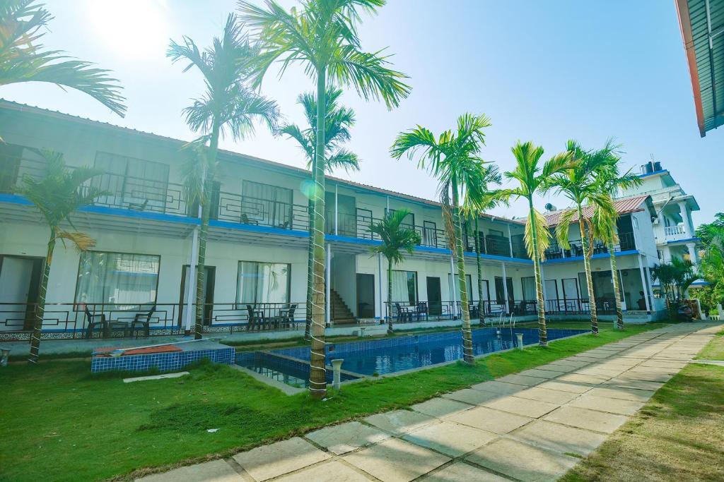 a building with palm trees and a swimming pool at FabHotel Morjim Bliss in Morjim