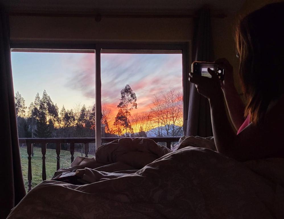 una mujer tomando una foto de una puesta de sol a través de una ventana en Casa Oriental en Cereceda
