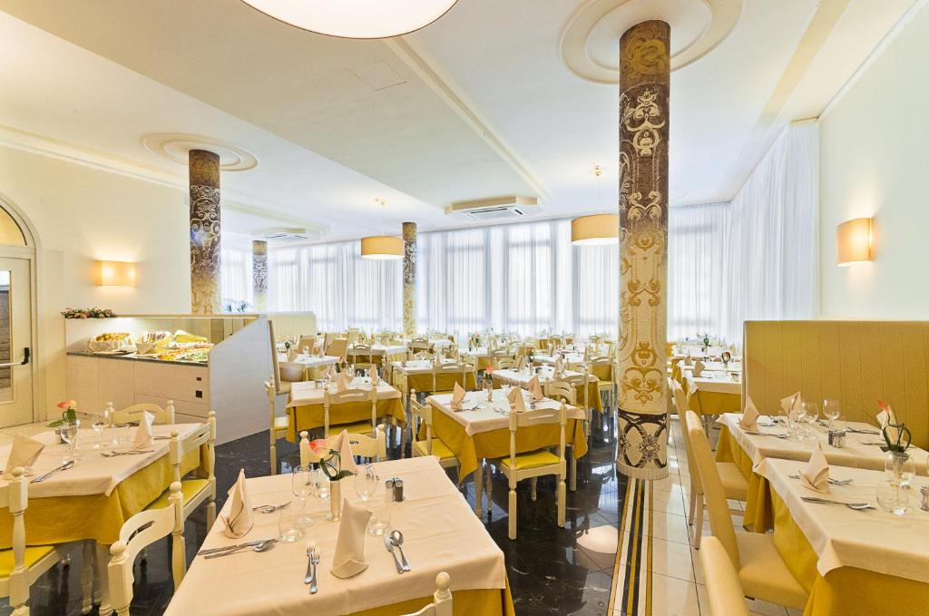a restaurant with white tables and yellow chairs at Hotel Montecarlo in Bibione