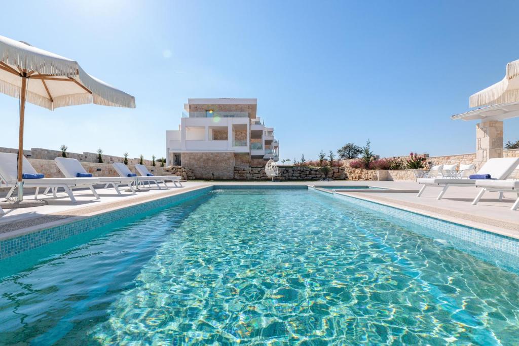 a swimming pool with chairs and an umbrella at Anna Mare Luxury Apartments in Afitos