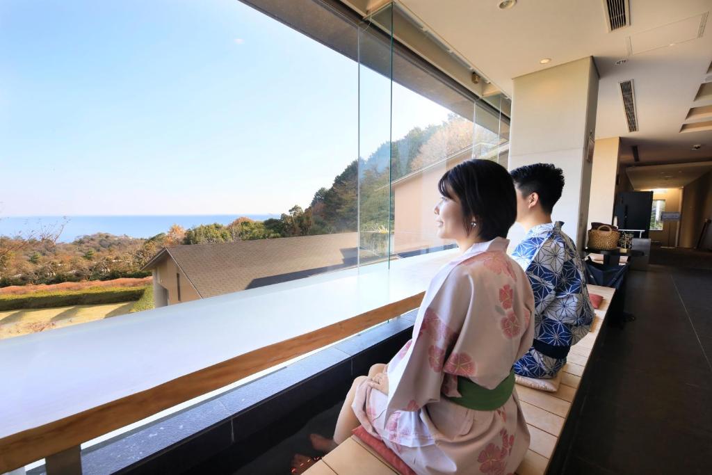duas pessoas sentadas numa varanda com vista para a janela em Yutorelo Atami em Atami