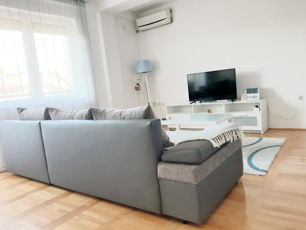 a living room with a gray couch and a tv at ASPERA Apartments in Kumanovo