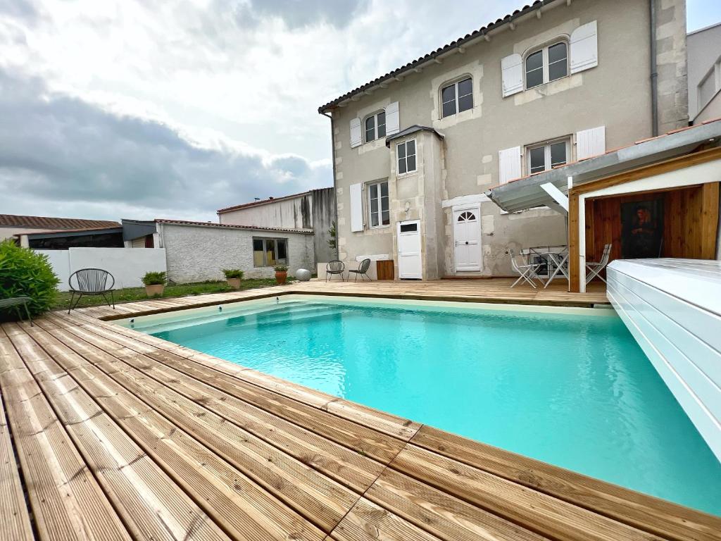 une piscine avec une terrasse en bois et une maison dans l'établissement La Sauvagère - Piscine, à La Rochelle