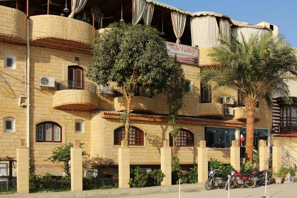 a yellow brick building with palm trees in front of it at Nile Valley Hotel in Luxor