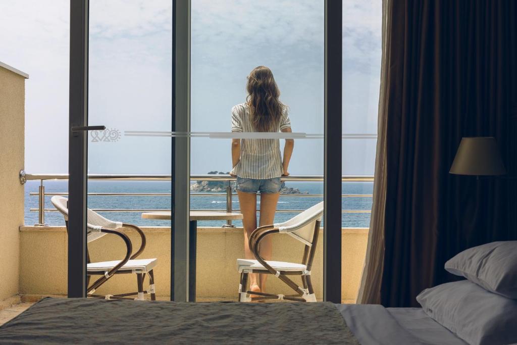 a woman looking out of a window at the ocean at Hotel Palas in Petrovac na Moru