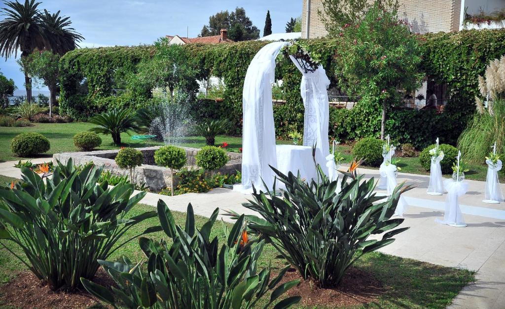 a white fountain in a garden with plants at Hotel Palas in Petrovac na Moru