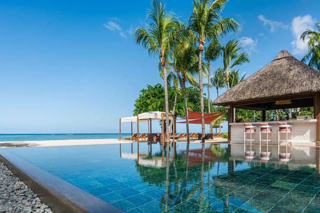 een zwembad naast een strand met palmbomen bij Hilton Mauritius Resort & Spa in Flic-en-Flac