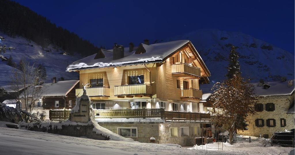 uma grande casa de madeira na neve à noite em Steinbock B&B - Apartaments em Livigno