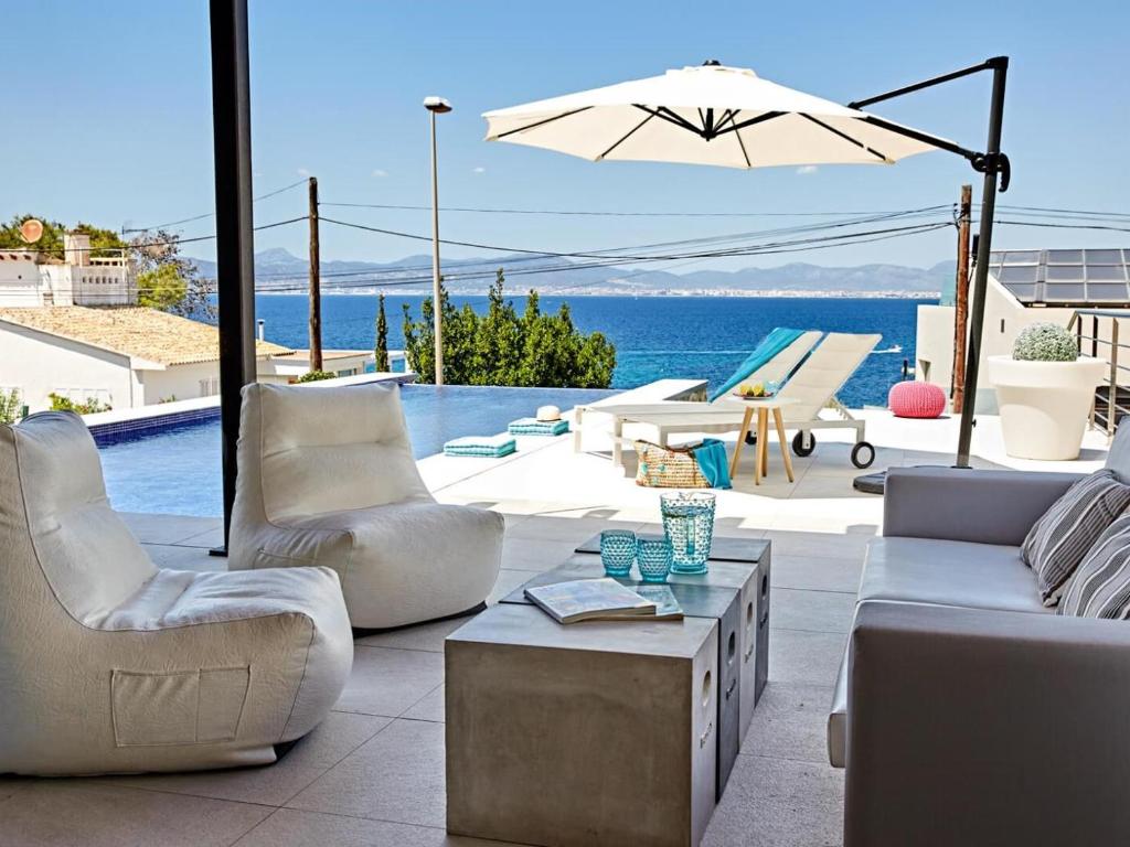 a patio with couches and an umbrella and the ocean at Villa Bellavista in Cala Blava