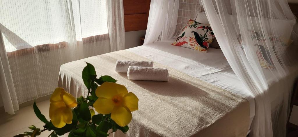 Una cama con colcha blanca y un jarrón con flores amarillas. en Casa noites tropicais en Imbassai