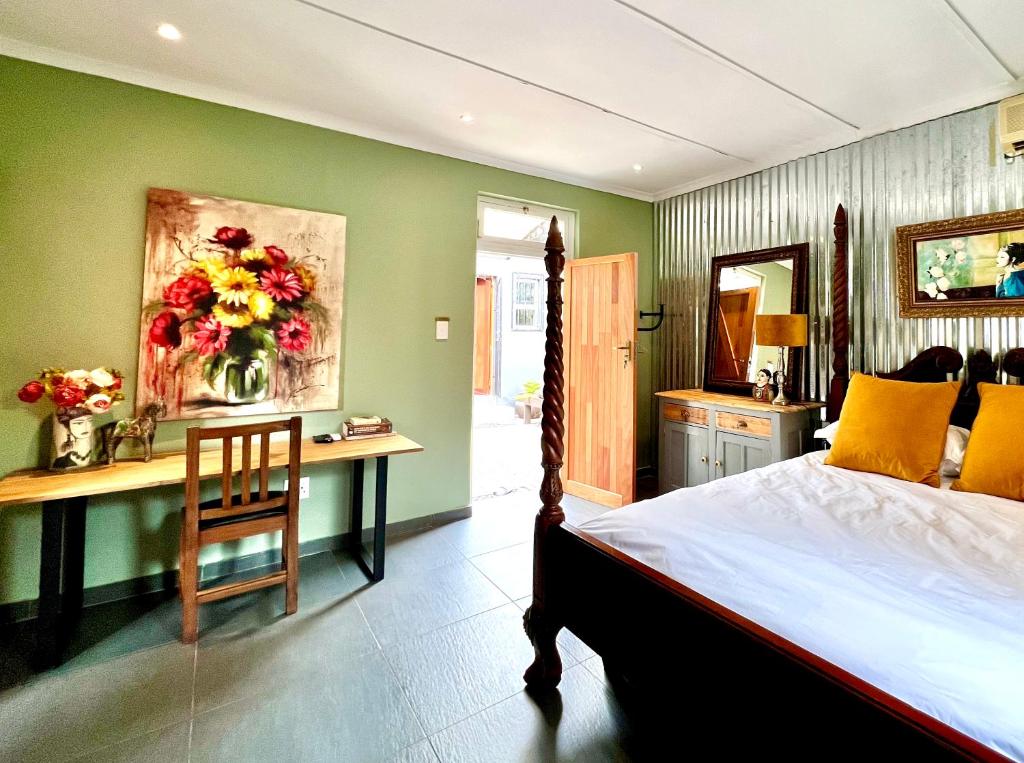 Terebinte Bed & Breakfast في ديربان: غرفة نوم مع سرير ومكتب مع إناء من الزهور
