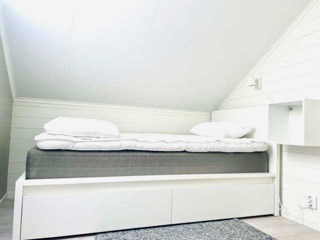 uma cama com lençóis brancos e almofadas num quarto em Bryggvingens Apartment 1 em Nösund