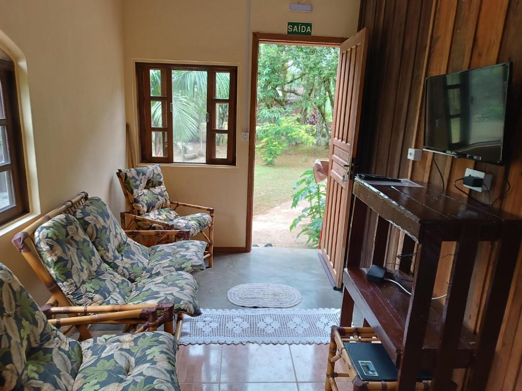 a living room with two chairs and a tv and a door at Pousada Serra Verde Ecolodges in Morretes