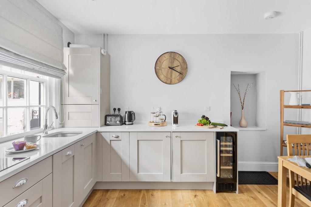 a kitchen with white cabinets and a clock on the wall at Higher Cottage with Parking in Dartmouth