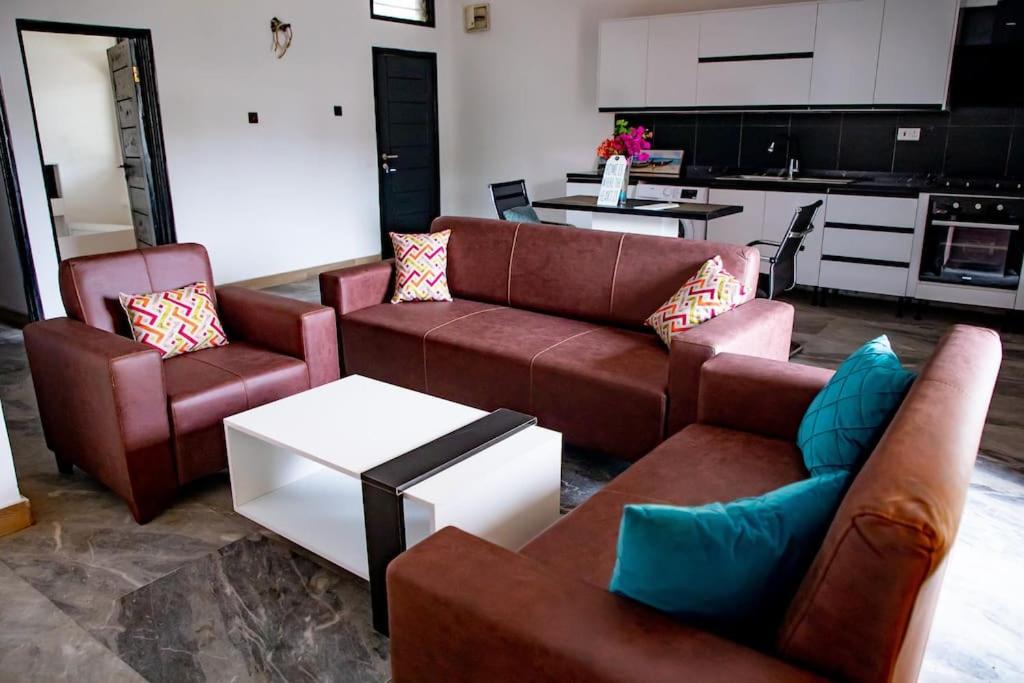 a living room with leather furniture and a kitchen at Cozy 1 Bed Apartment East Legon in Bawaleshi
