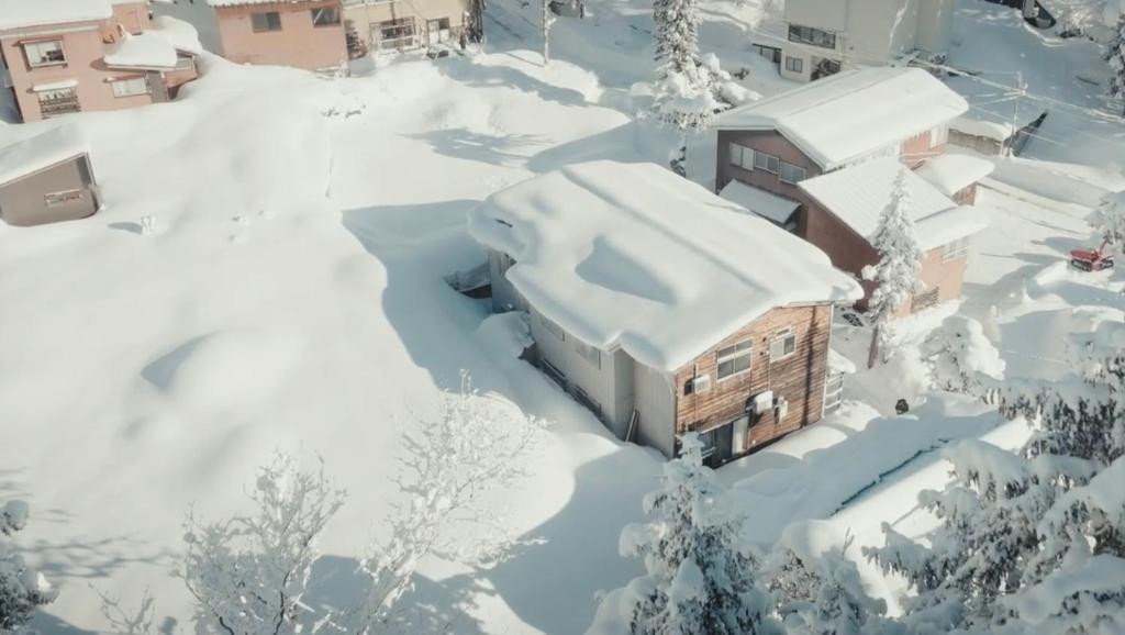 una casa cubierta de nieve con árboles y edificios en The Greenhouse, en Myoko