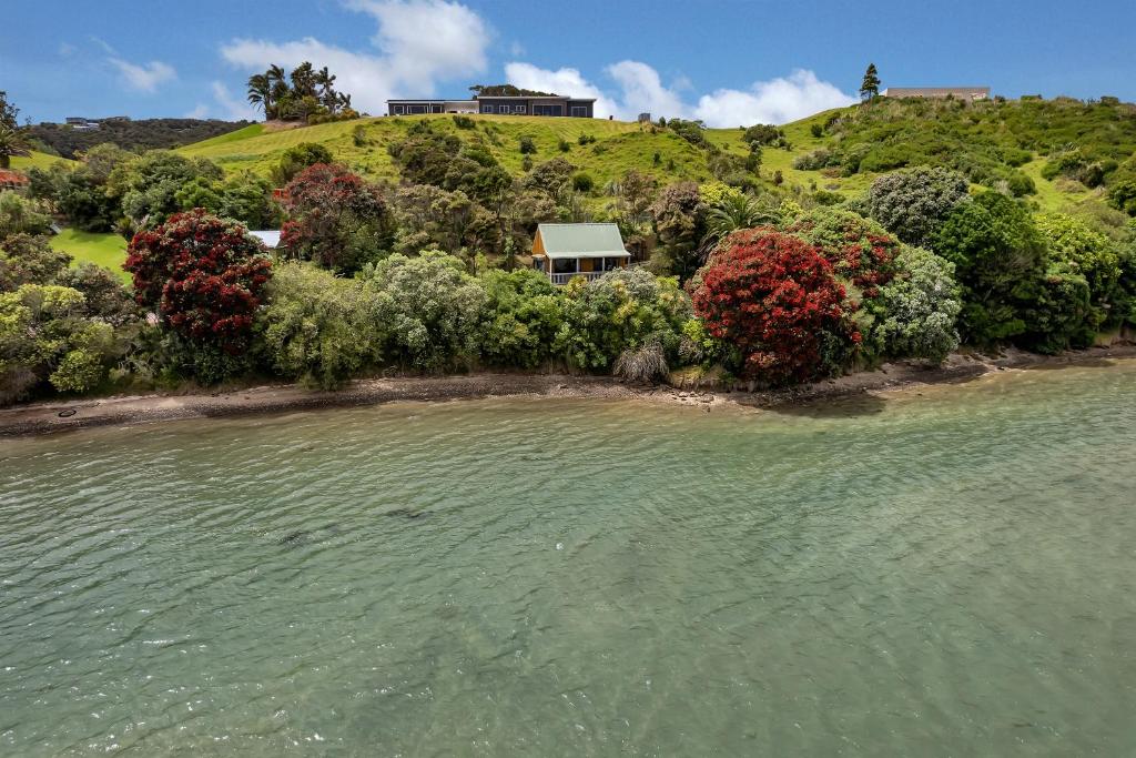 a house on a hill next to a body of water at Macrocarpa Cottage - Cable Bay Holiday Home in Cable Bay