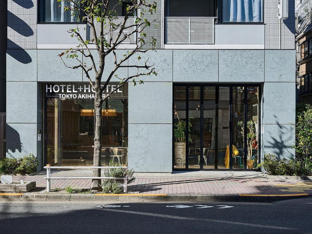 einen Hoteleingang mit einem Baum vor einem Gebäude in der Unterkunft Hotel Plus Hostel TOKYO AKIHABARA in Tokio