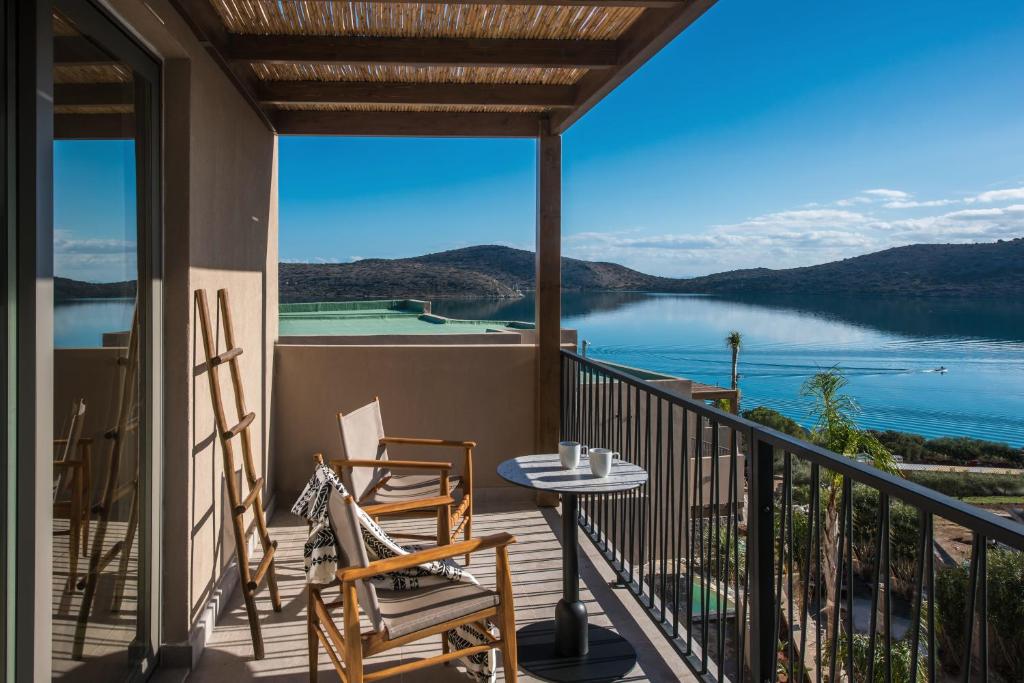 een balkon met stoelen en een tafel met uitzicht op een meer bij Elounda Infinity Exclusive Resort & Spa - Adults Only in Elounda