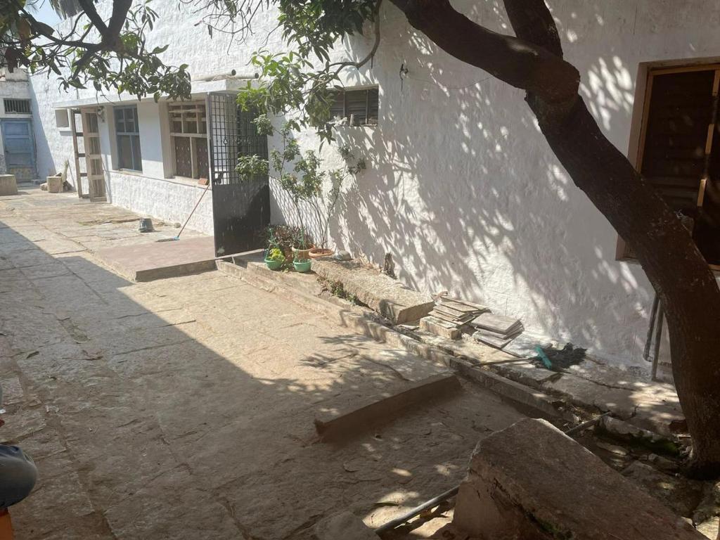 a white building with a tree next to a sidewalk at Hampi backyard vibes in Hospet