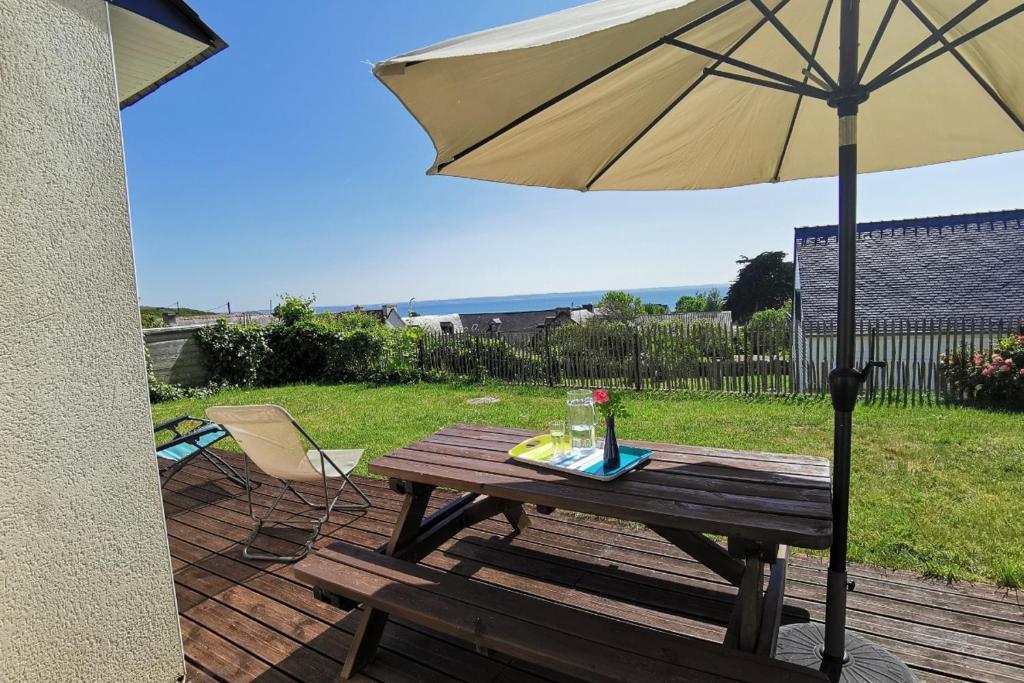 - une table en bois avec un parasol sur la terrasse dans l'établissement Capucines et agapanthes, à Saint-Nic