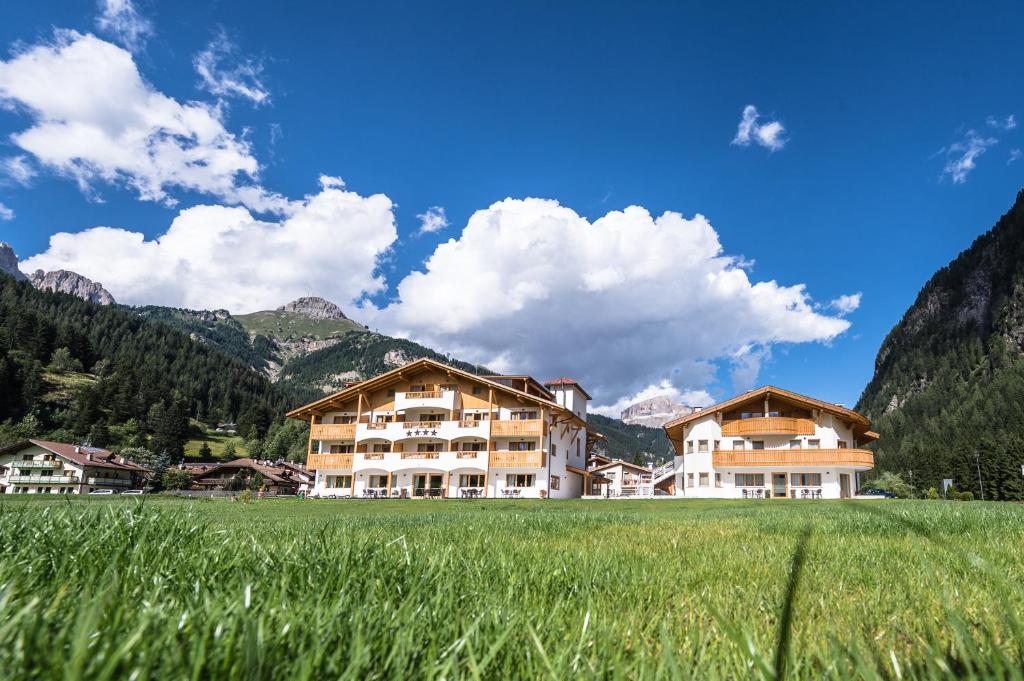 a building in a field with mountains in the background at Golden Park Resort in Campitello di Fassa
