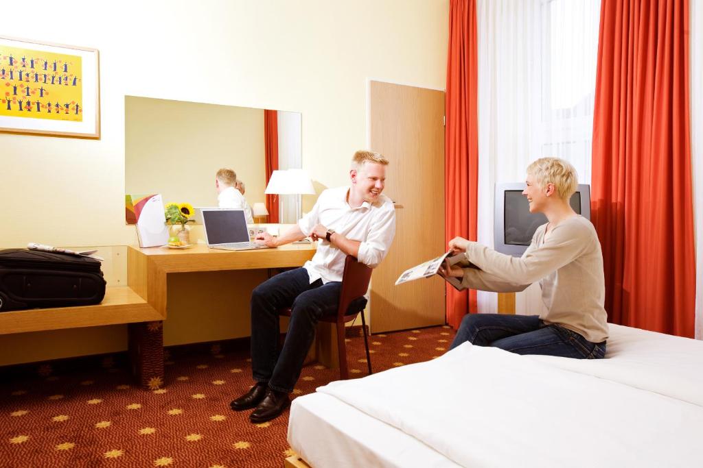two men sitting at a desk in a hotel room at Vienna House Easy by Wyndham Rostock in Rostock