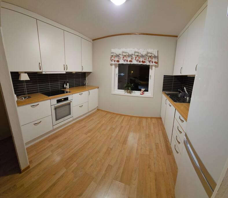 a kitchen with white cabinets and a wooden floor at Tønsvik enebolig in Tromsø