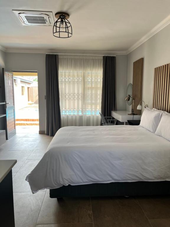 a bedroom with a large white bed and a desk at Casero Guesthouse in Klerksdorp