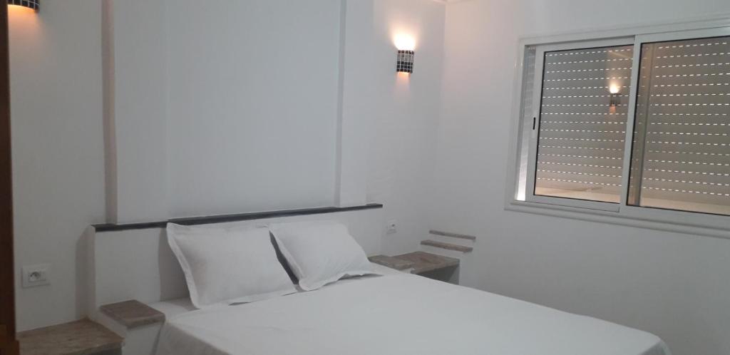 a white bedroom with a bed and a window at Beach Houses in Sfax