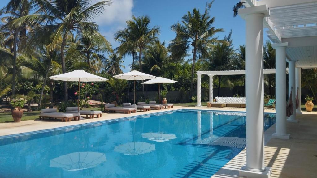 Maxaranguape的住宿－Maracajau Luxury Home - Villa-Mar-a-Villa，一个带椅子和遮阳伞的游泳池