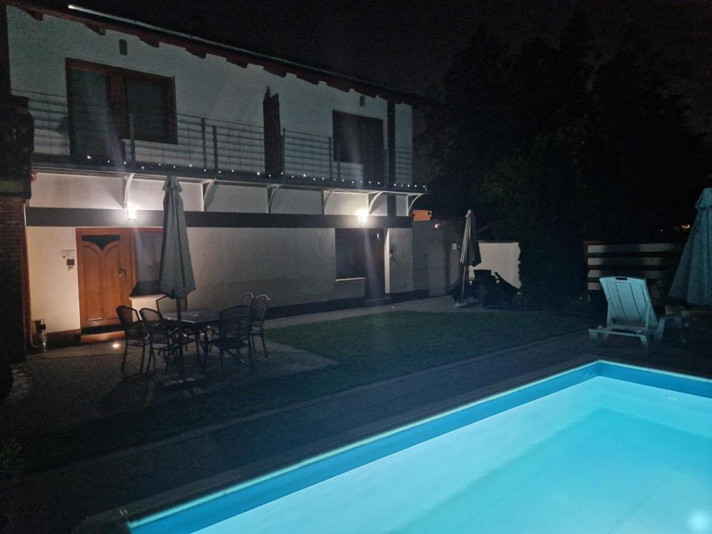 a swimming pool at night with chairs and umbrellas at Martina apartman in Gyula
