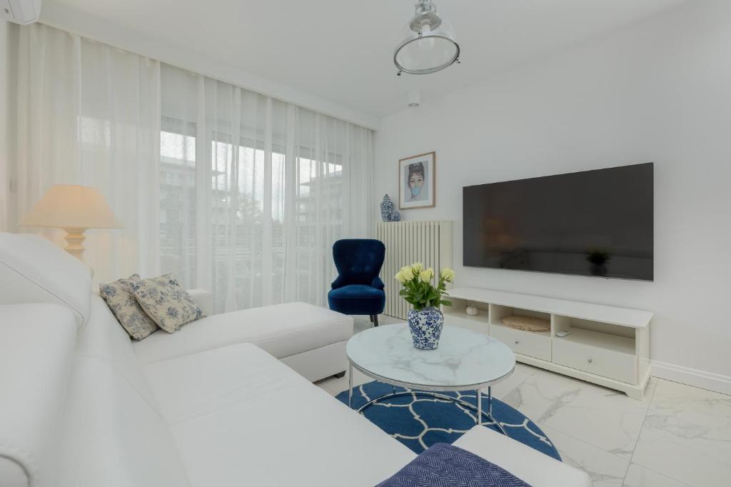 ein Wohnzimmer mit einem weißen Sofa und einem Fernseher in der Unterkunft Apartament Ambra Marina - Basen & SPA in Dziwnów