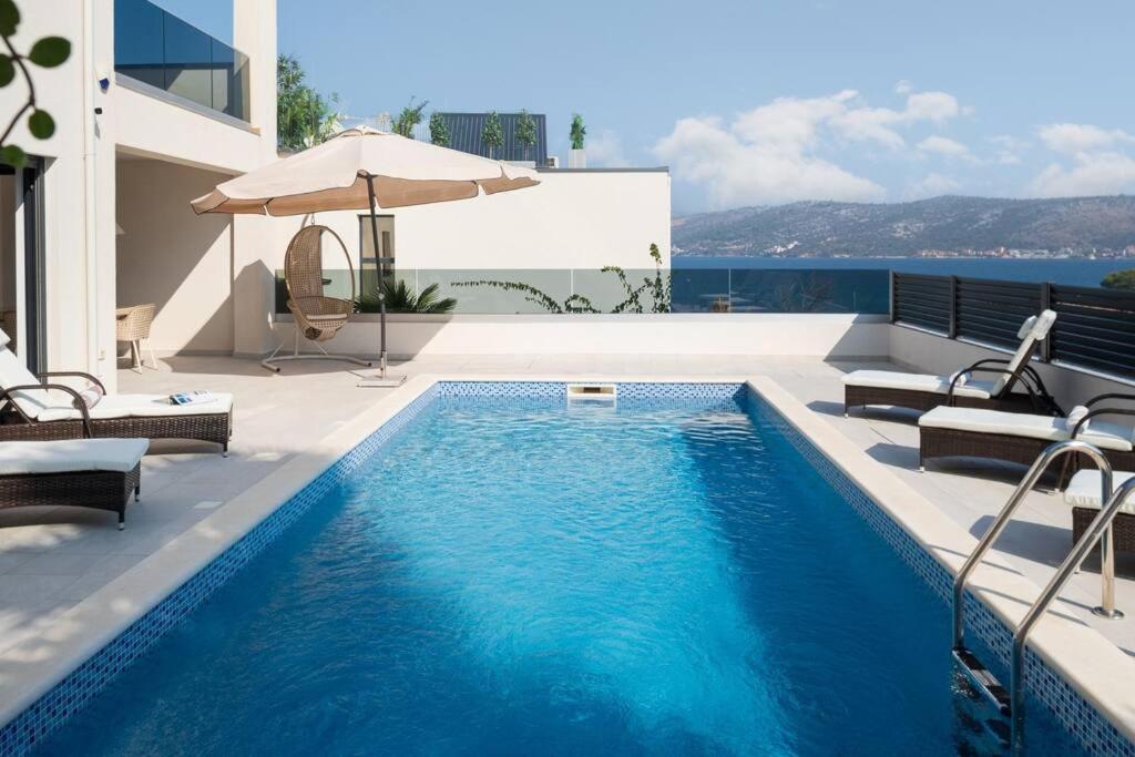 a swimming pool with chairs and an umbrella next to a house at Villa Palm Bay 2, heated pool - 10 m from the sea in Ražanj