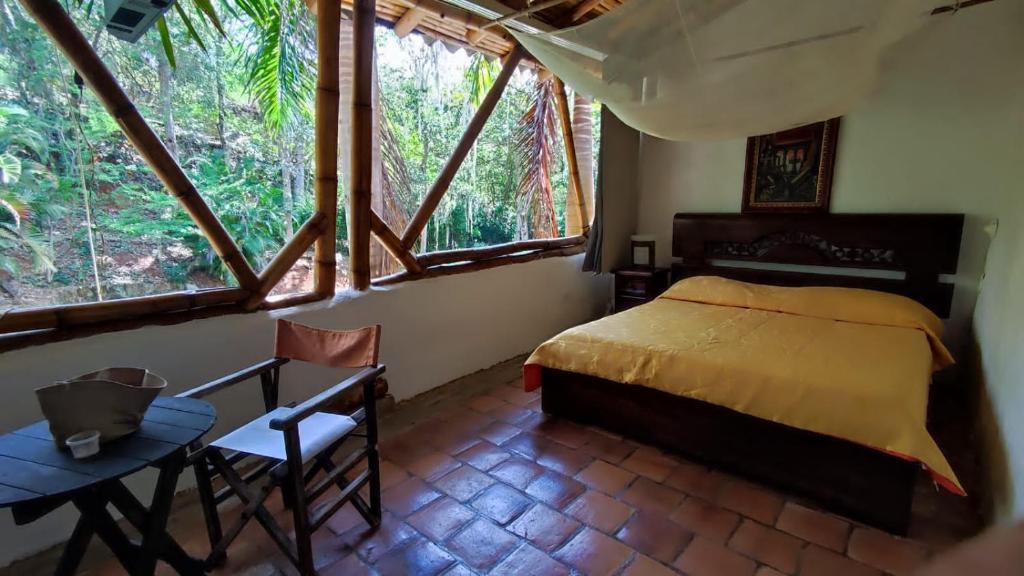 1 dormitorio con cama, mesa y ventanas en Cabañas Coloniales con Entorno Natural en Barichara en Barichara