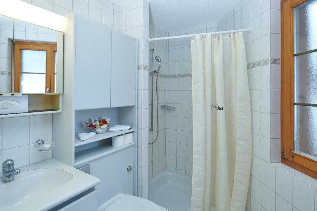 baño blanco con ducha y lavamanos en Hotel Central Wolter - Grindelwald, en Grindelwald