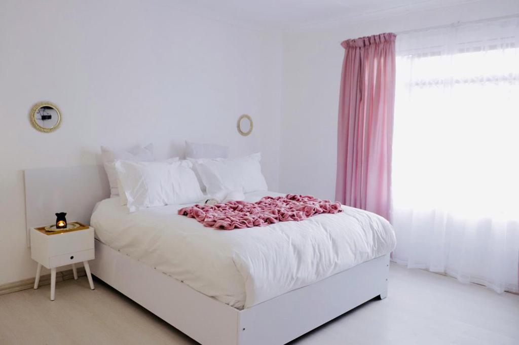 a white bedroom with a white bed with pink flowers on it at Lake Acres Guest House in Kokstad