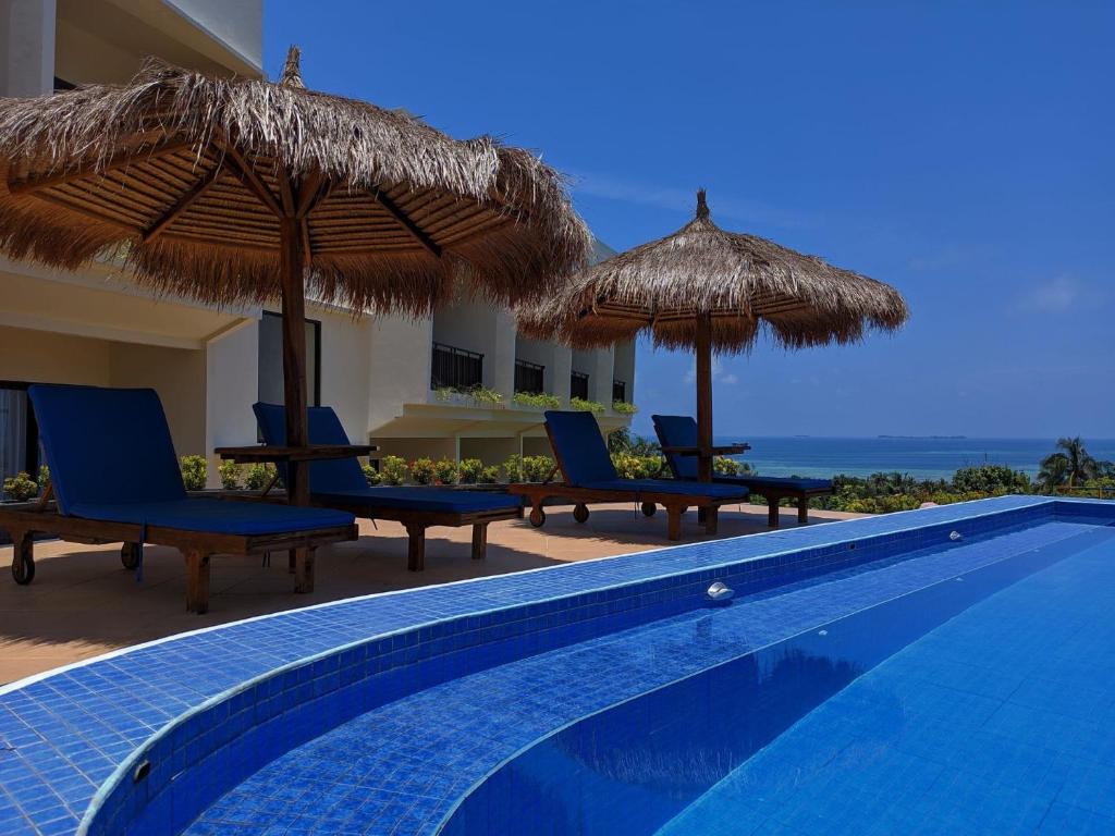 a swimming pool with chairs and umbrellas and the ocean at The Happinezz Hills Hotel in Karimunjawa