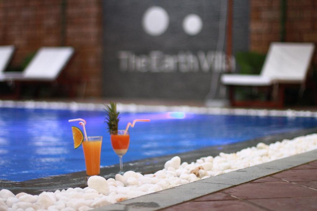two cocktails sitting on a ledge next to a swimming pool at The Earth Villa in Hoi An