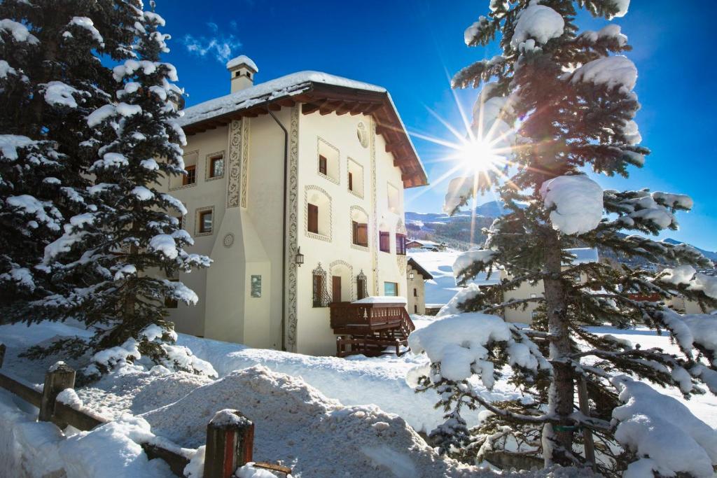 un edificio en la nieve con un árbol y el sol en White Pine Lodge Livigno en Livigno