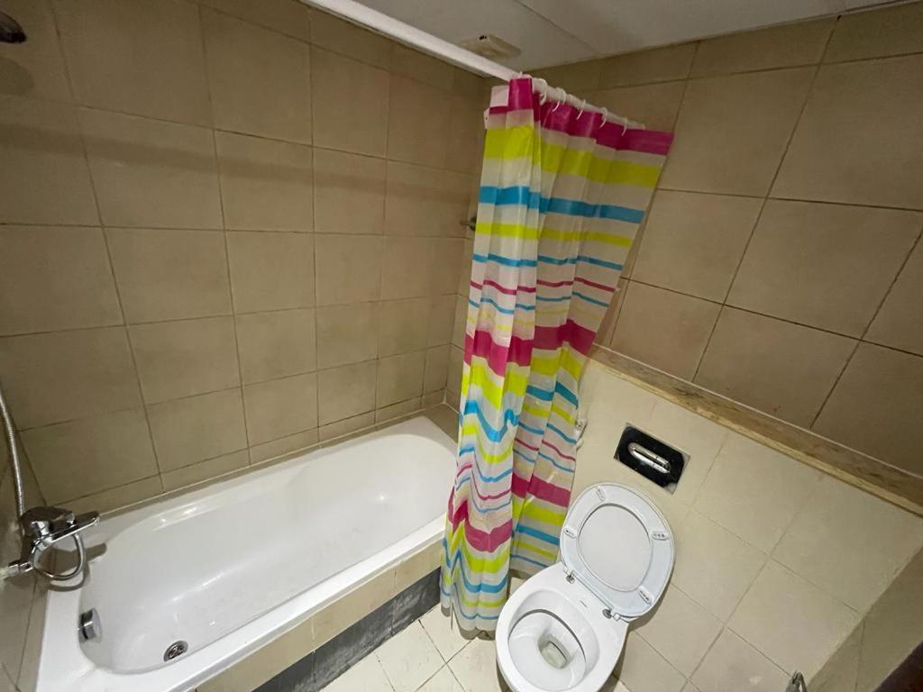 La salle de bains est pourvue d'une baignoire, de toilettes et d'un rideau de douche. dans l'établissement Tidy Partition with Window and TV close to MOE, à Dubaï
