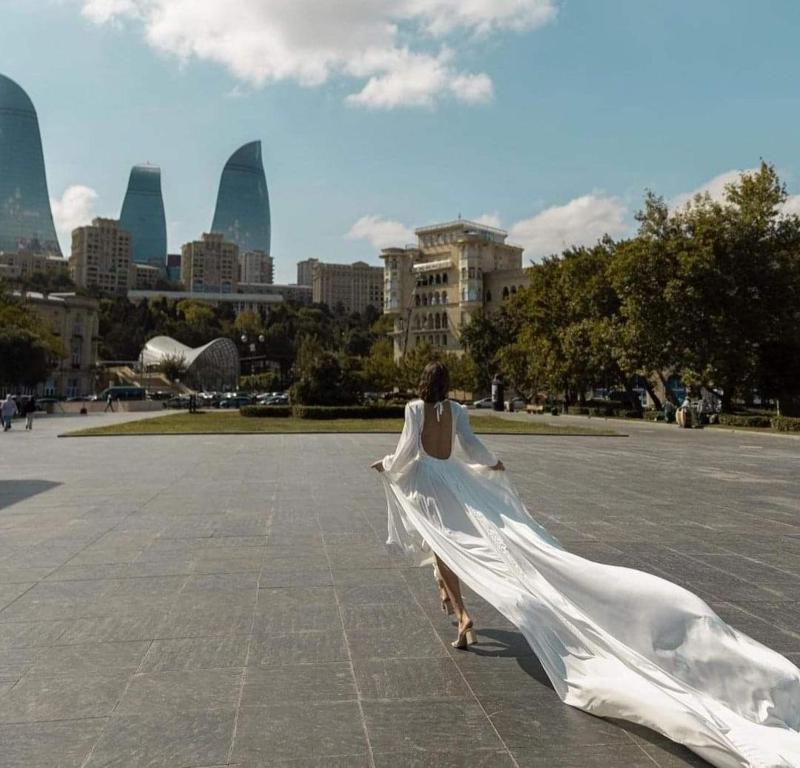 Una mujer vestida de blanco caminando delante de una ciudad en Eminera Hostels Baku en Bakú