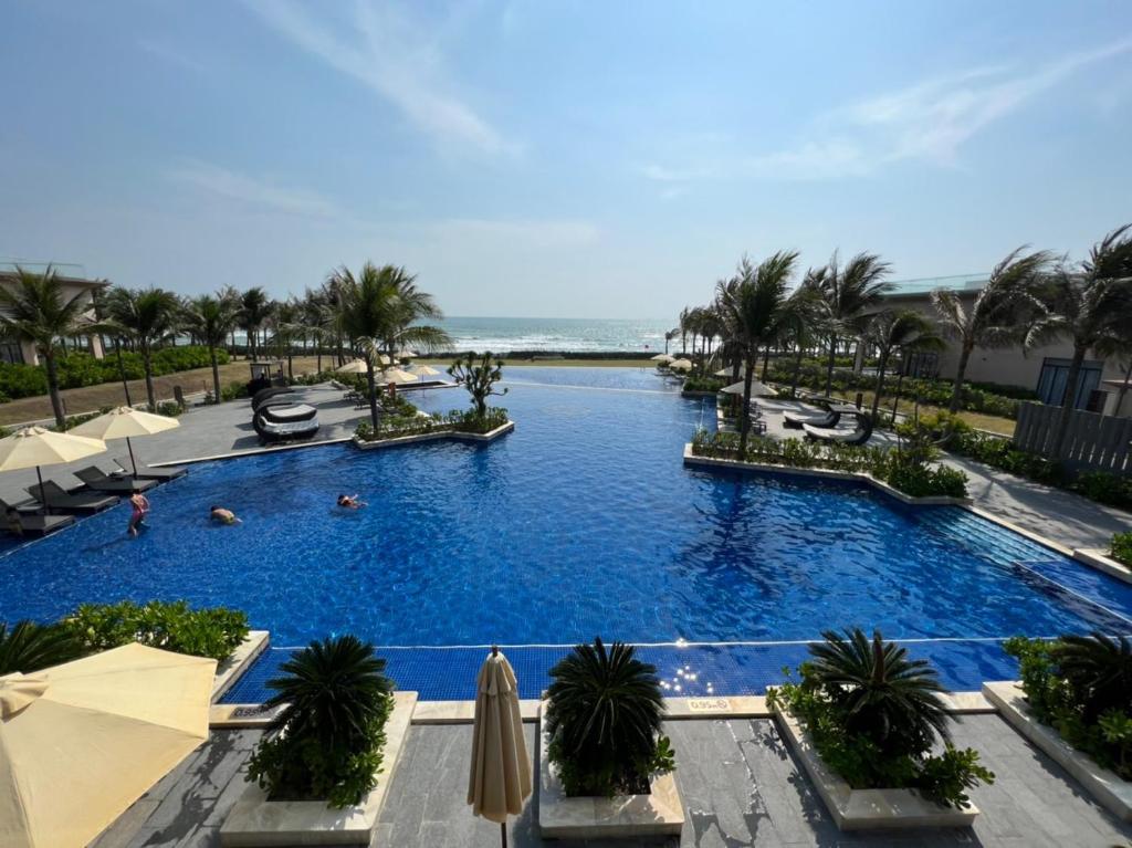a large swimming pool with palm trees and the ocean at Wyndham Cam Ranh Villa 1412 in Cam Lâm