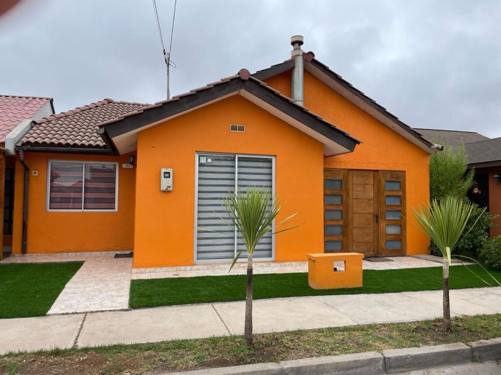 pomarańczowy dom z dwoma palmami przed nim w obiekcie Amplia Casa en Condominio w mieście La Serena