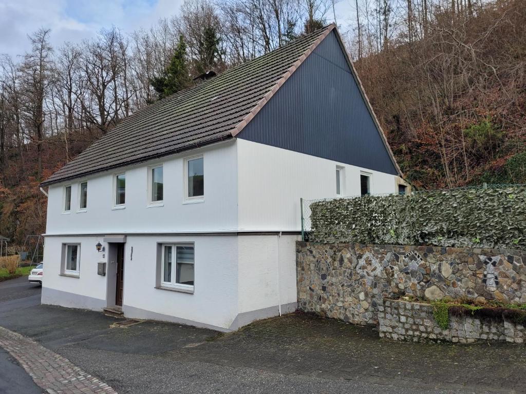 a white house with a black roof and a stone wall at Familyhome Lopora in Medebach