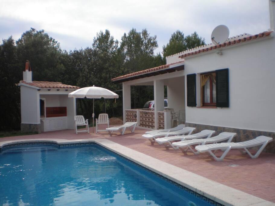 een huis met een zwembad met stoelen en een parasol bij Villa en Sa Roca in Es Mercadal