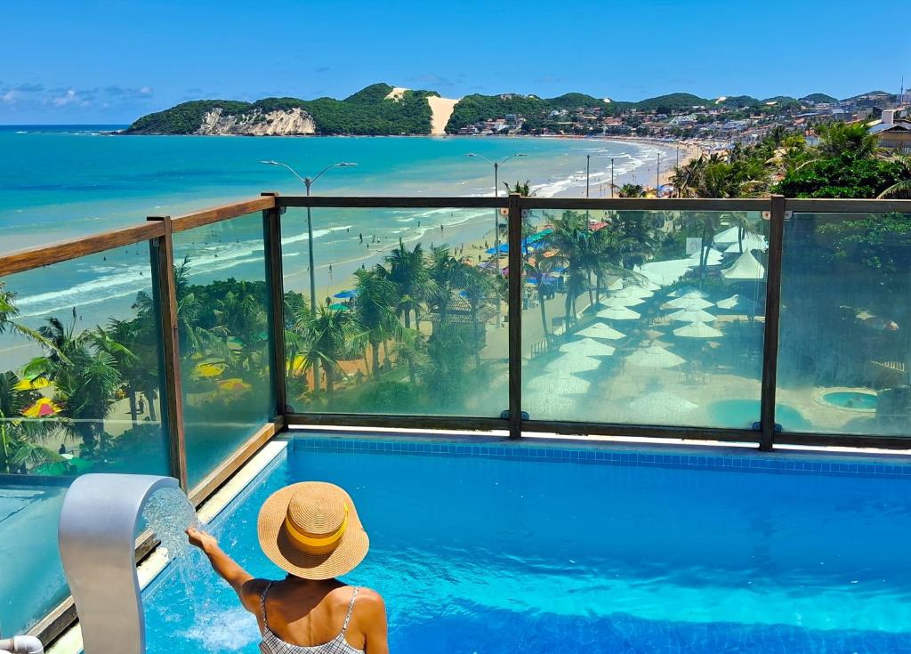 kobieta w kapeluszu siedząca w basenie patrząca na ocean w obiekcie Araça flat 308 - Lateral Vista Jardim w mieście Natal