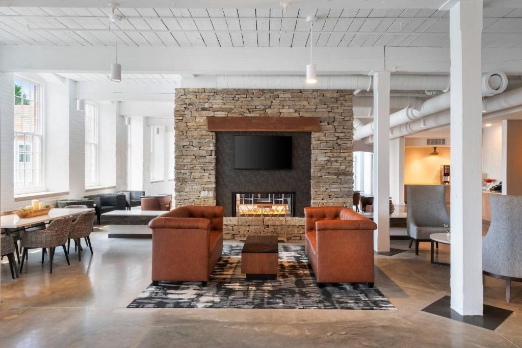 a lobby with a brick fireplace with chairs and tables at Fairfield Inn & Suites Madison Historic Eagle Cotton Mill in Madison