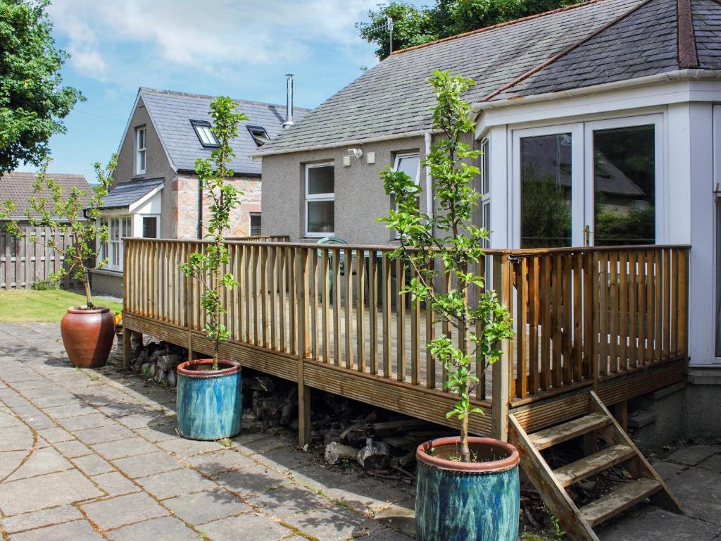 a house with two potted trees in barrels next to a fence at Pine Tree Cottage - Uk45925 in Ballater