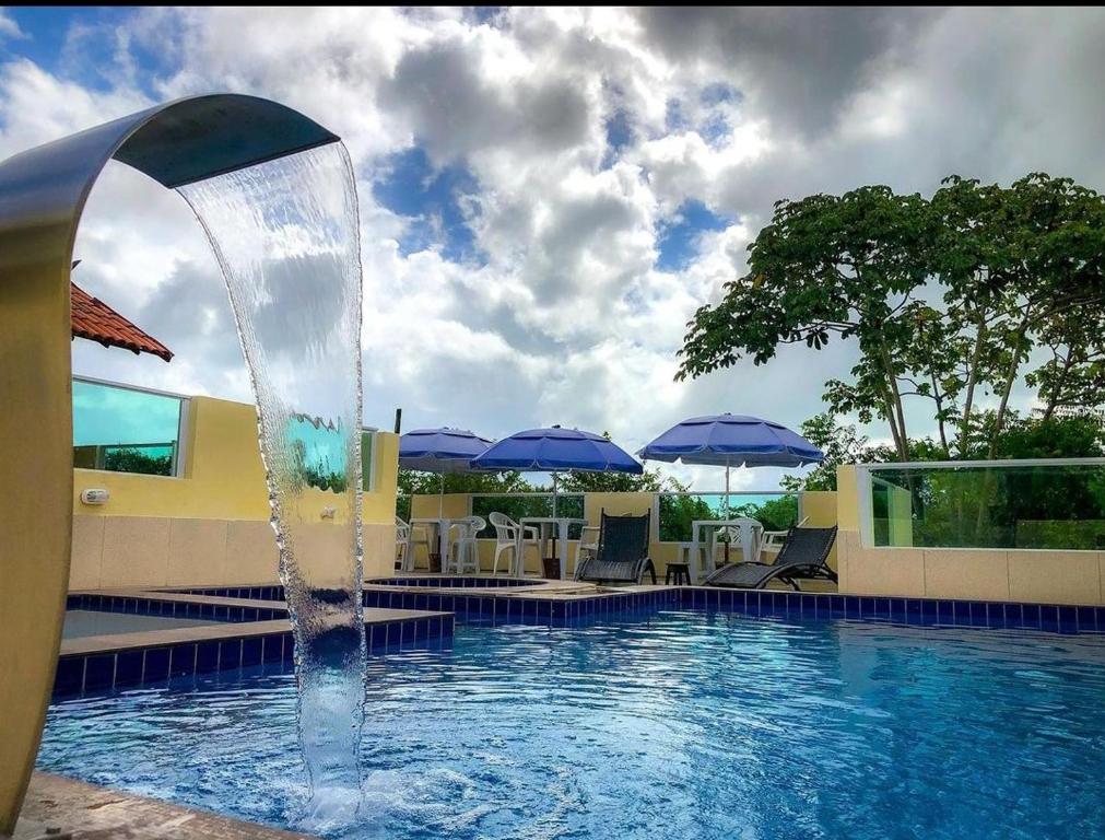 une fontaine dans une piscine avec des chaises et des parasols dans l'établissement Villa Velha Flats, à Itamaracá